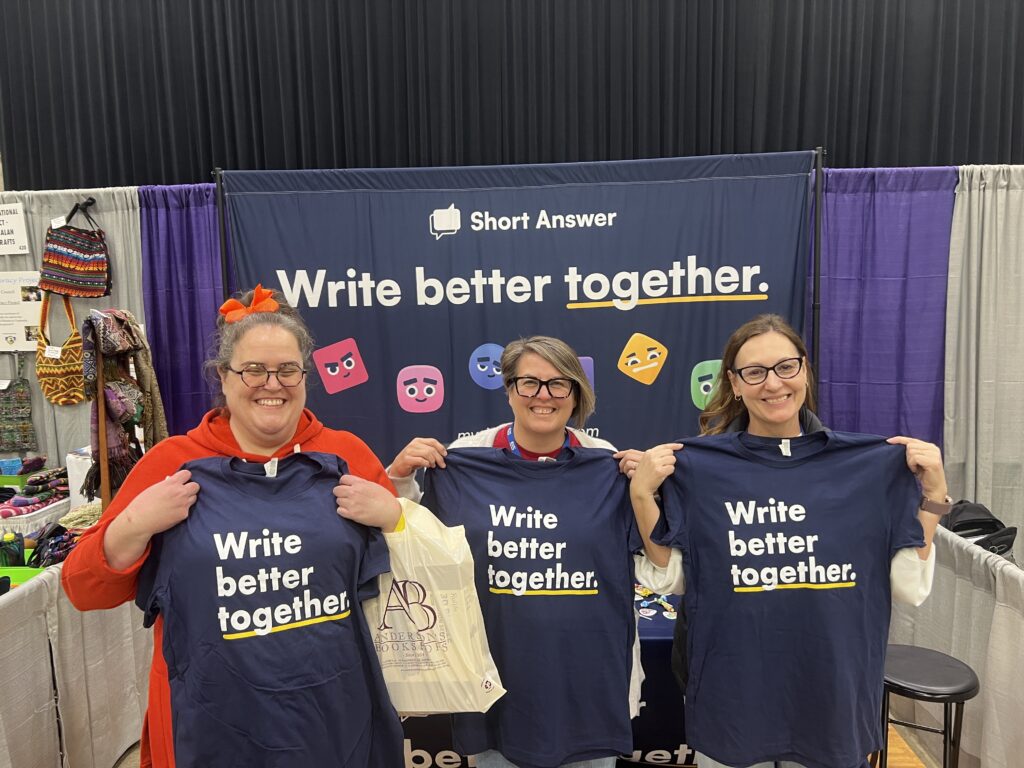 Educators holding up t shirts at the Short Answer booth